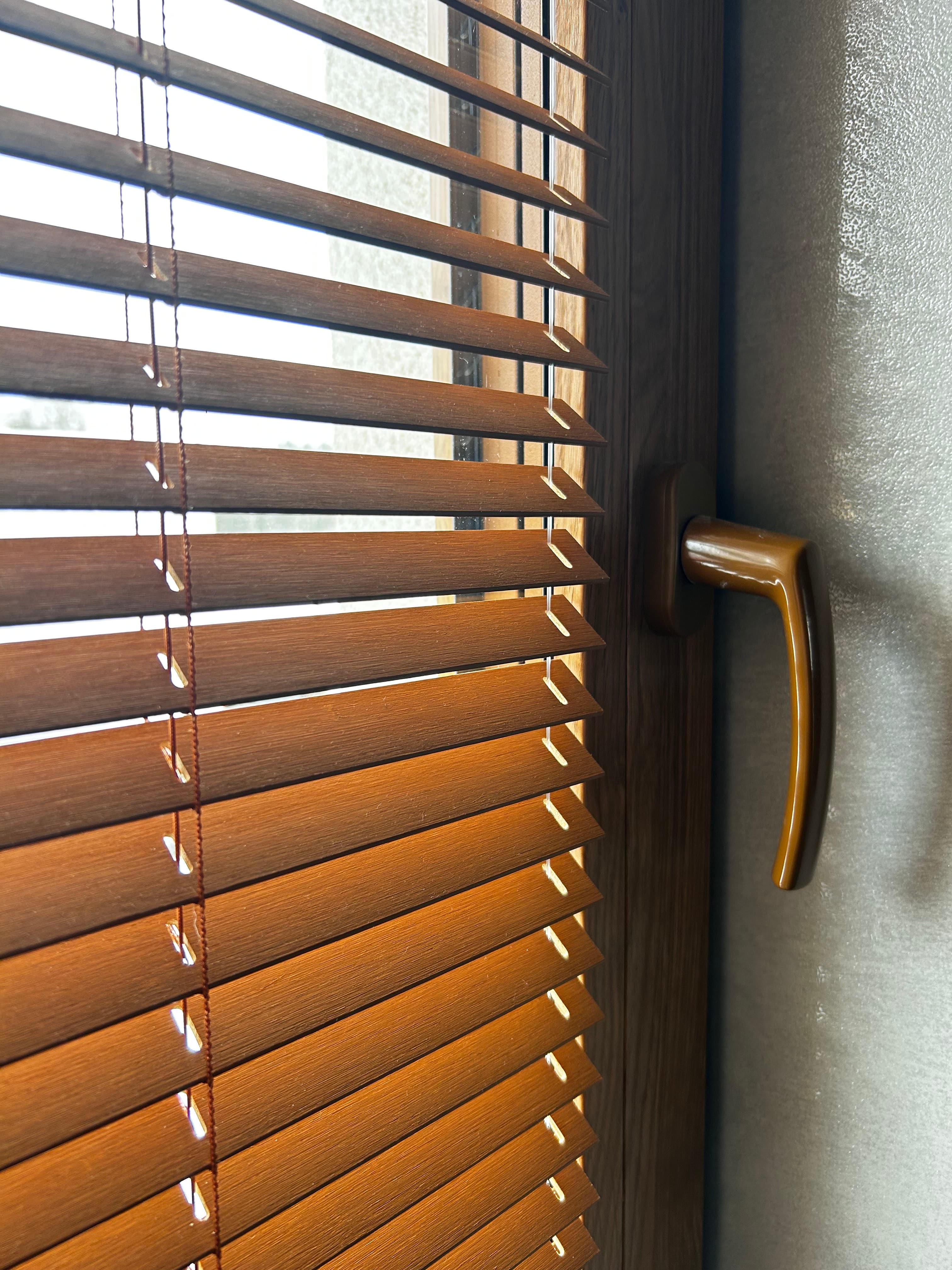 Sunlight filtering through horizontal wooden blinds below a curved bronze handle on a window frame.