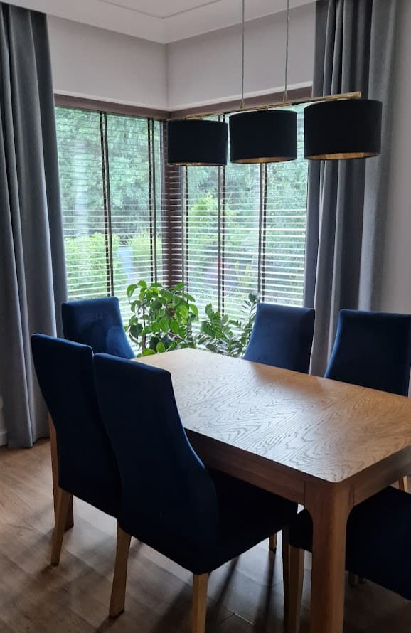 Light wood dining table with navy velvet chairs beneath a black triple pendant light.